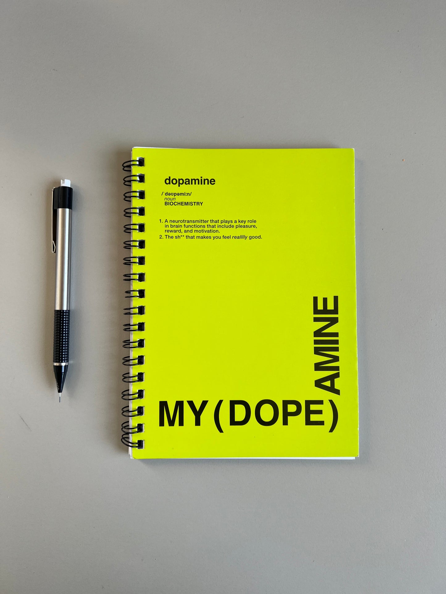 Yellow notebook with black text and a pen on a gray background